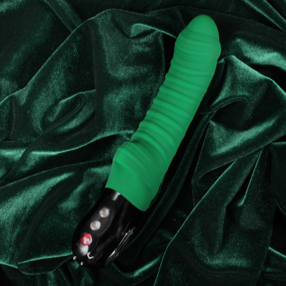 Green ribbed massager with black base and buttons on dark green velvet.