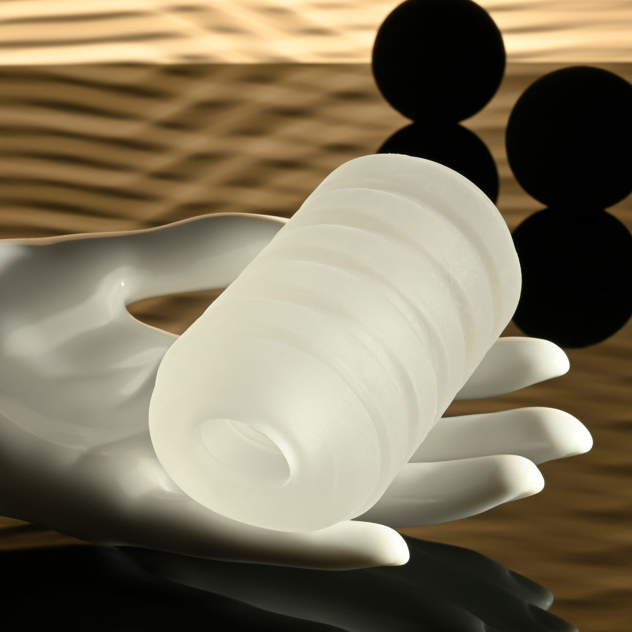 Frosted white ribbed stroker held in a white hand with black spheres in the background.