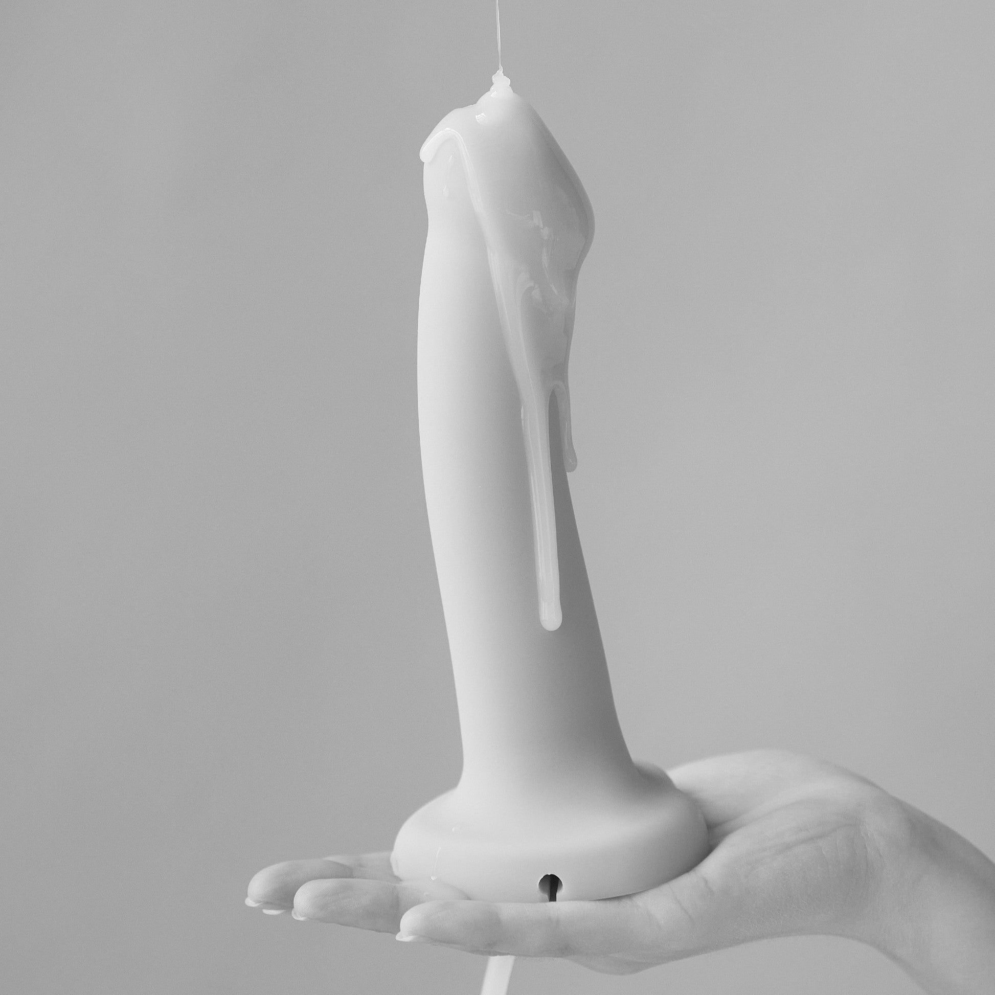 A hand holds a white, phallic-shaped object with milky gel dripping from the top.