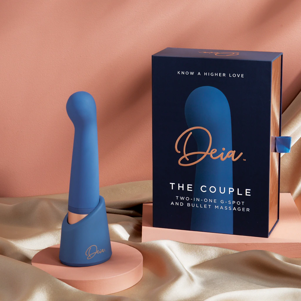 A blue dual motor vibrator with a charging stand and its box.