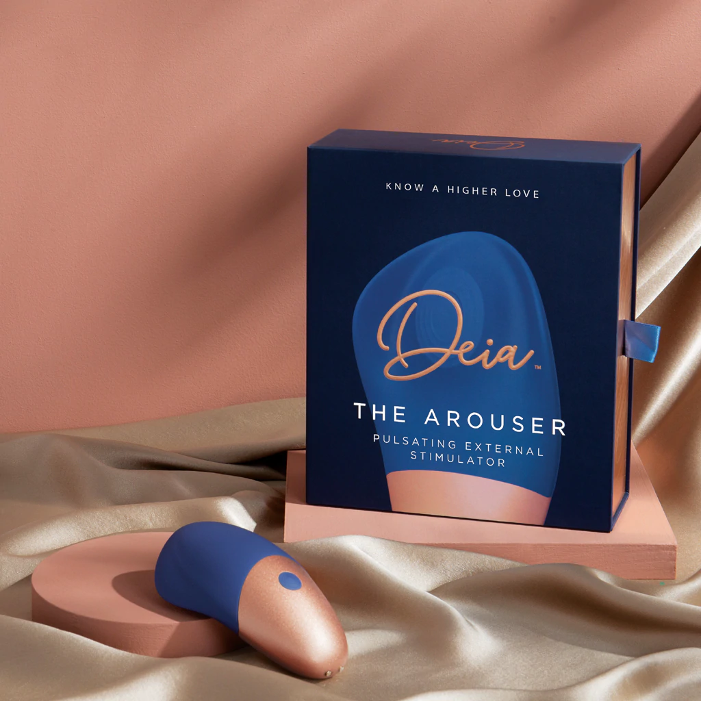 A blue and rose gold Deia wand massager sits next to its navy blue box.