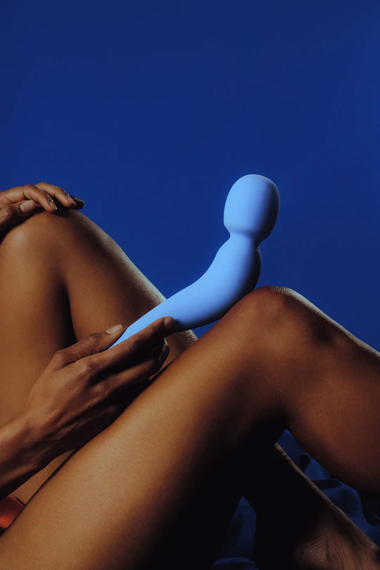 Periwinkle silicone wand vibrator held by hands against legs.