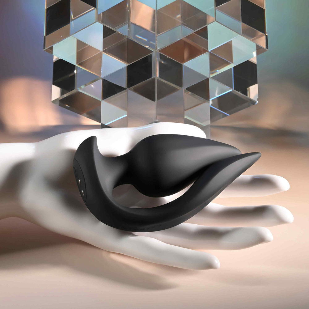 Black dual motor silicone plug on a white hand with a geometric sculpture.