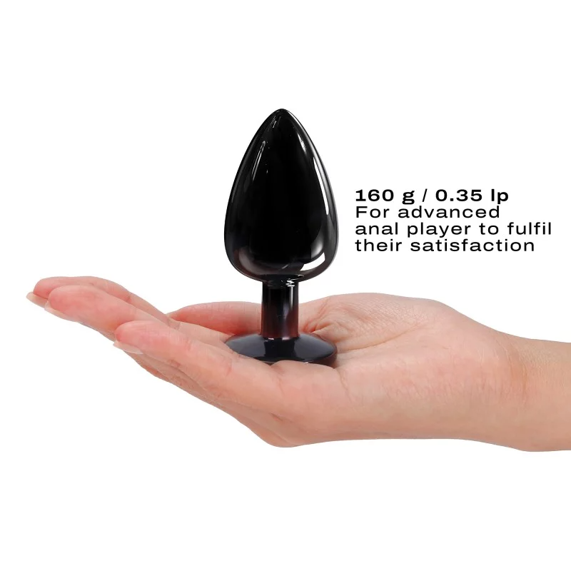 A large black metal anal plug with a diamond-shaped base rests on a hand.