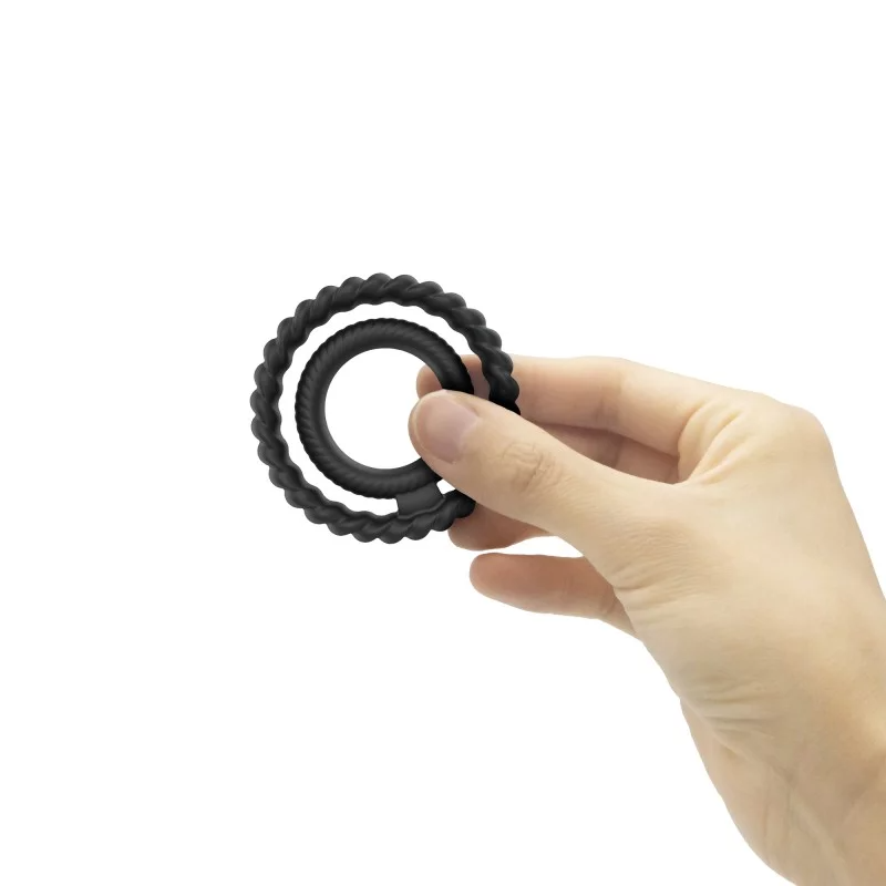 A hand holds two black silicone rings, one inside the other.