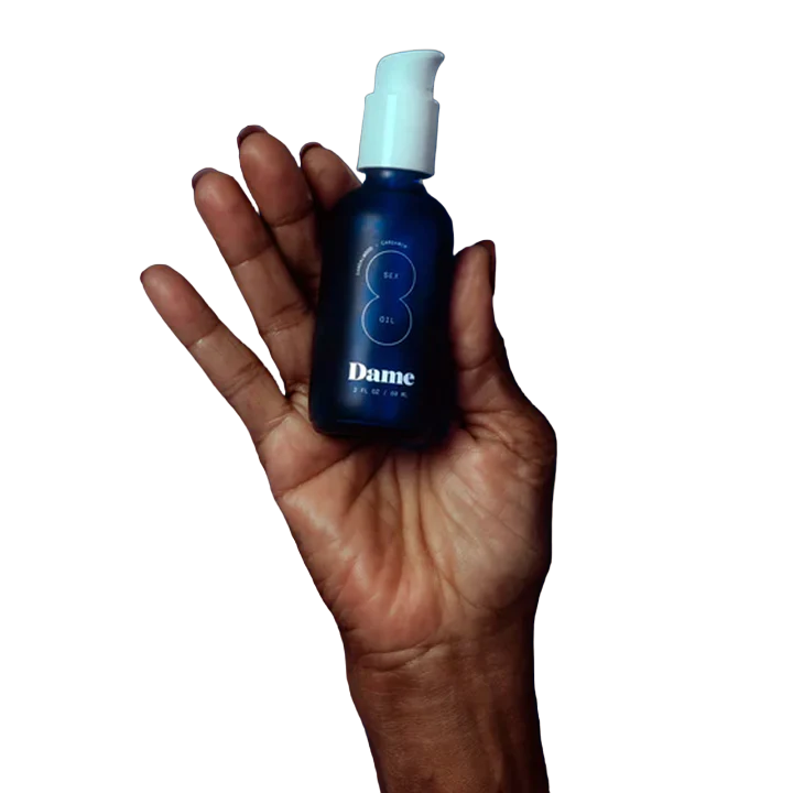A blue bottle of Dame Sex Oil with a white pump held in a hand.