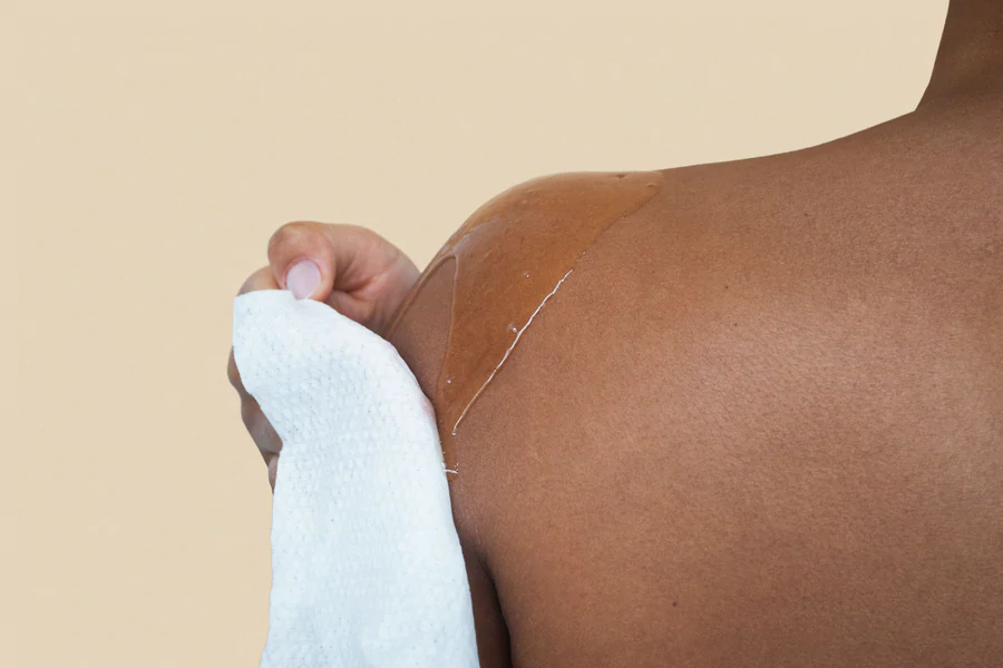 A hand holds a white wipe to a shoulder with a clear gel.