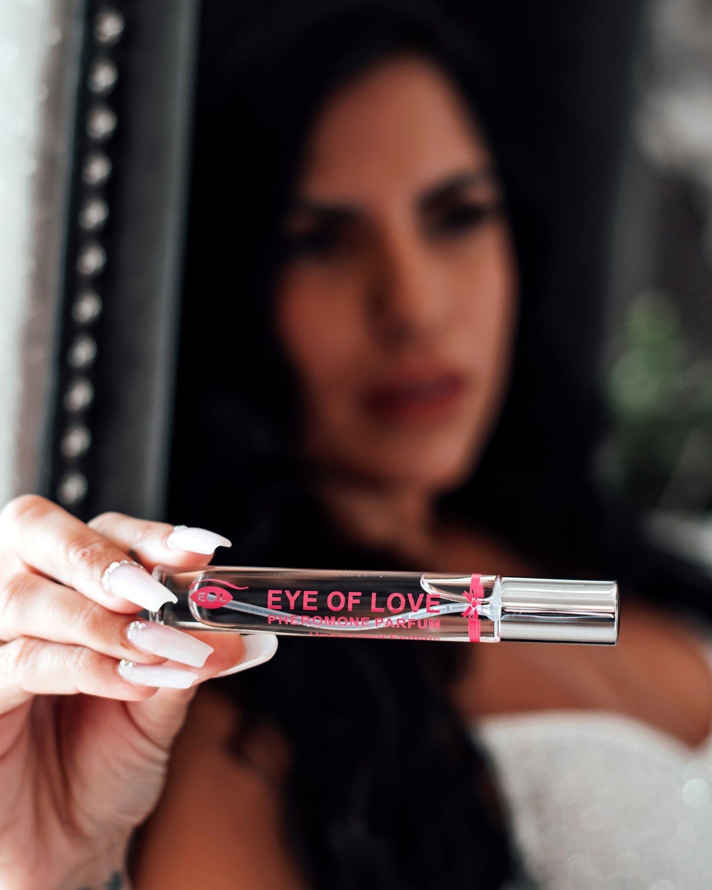 A woman holds a rollerball bottle of Eye of Love pheromone parfum.
