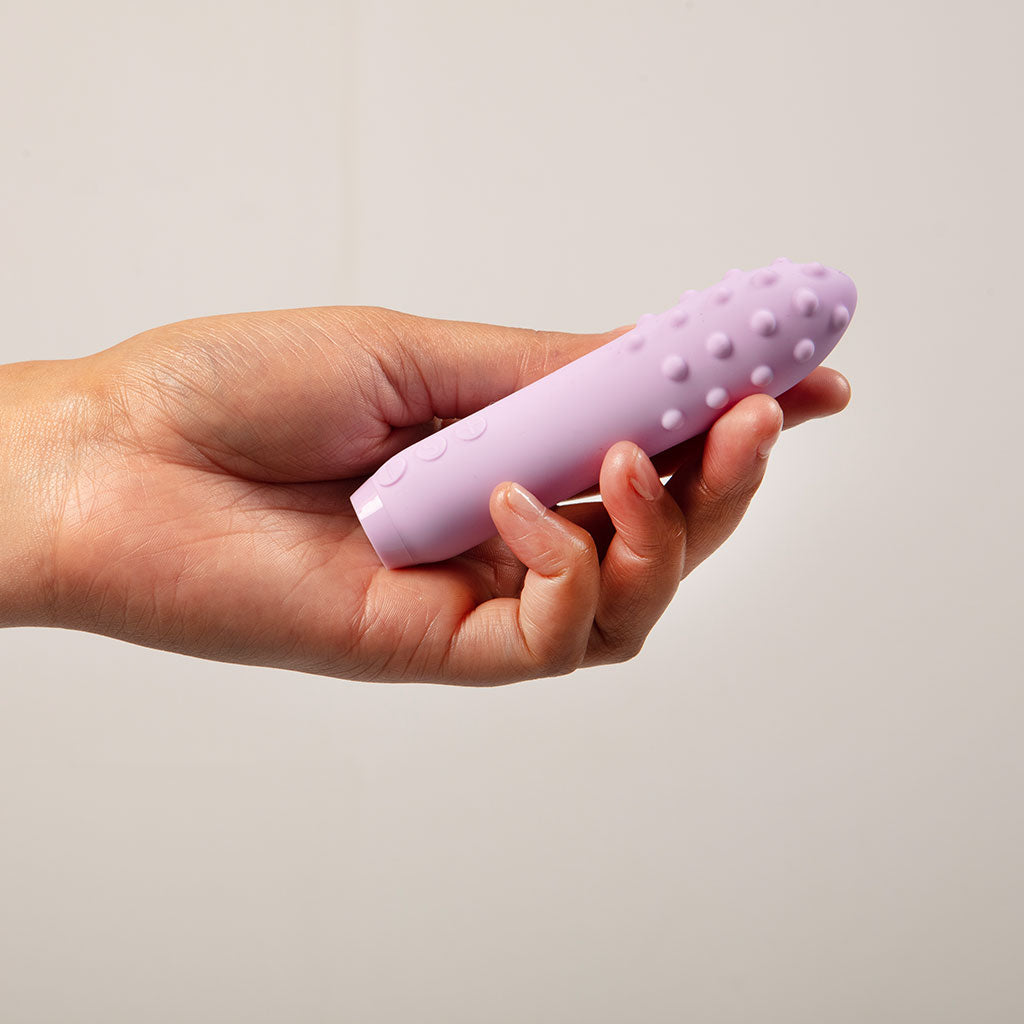 A lilac silicone vibrator with raised bumps held in a hand.