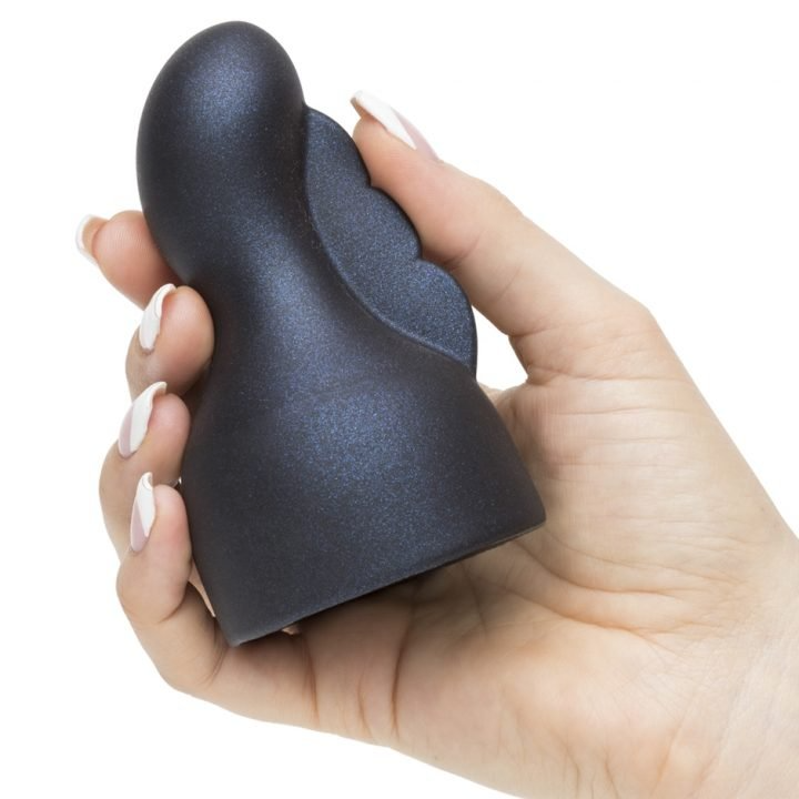 A hand holds a dark gray clitoral flutter wand attachment with a scalloped edge.