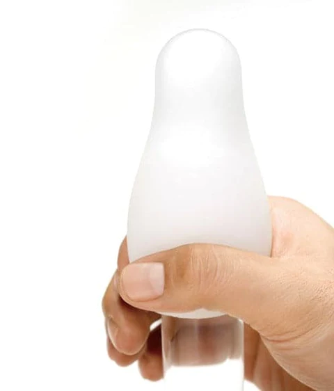 A hand holds a white, ribbed Tenga masturbator egg.