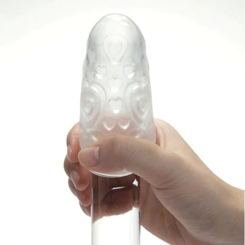 A clear, textured male pleasure sleeve with heart patterns, held by a hand.