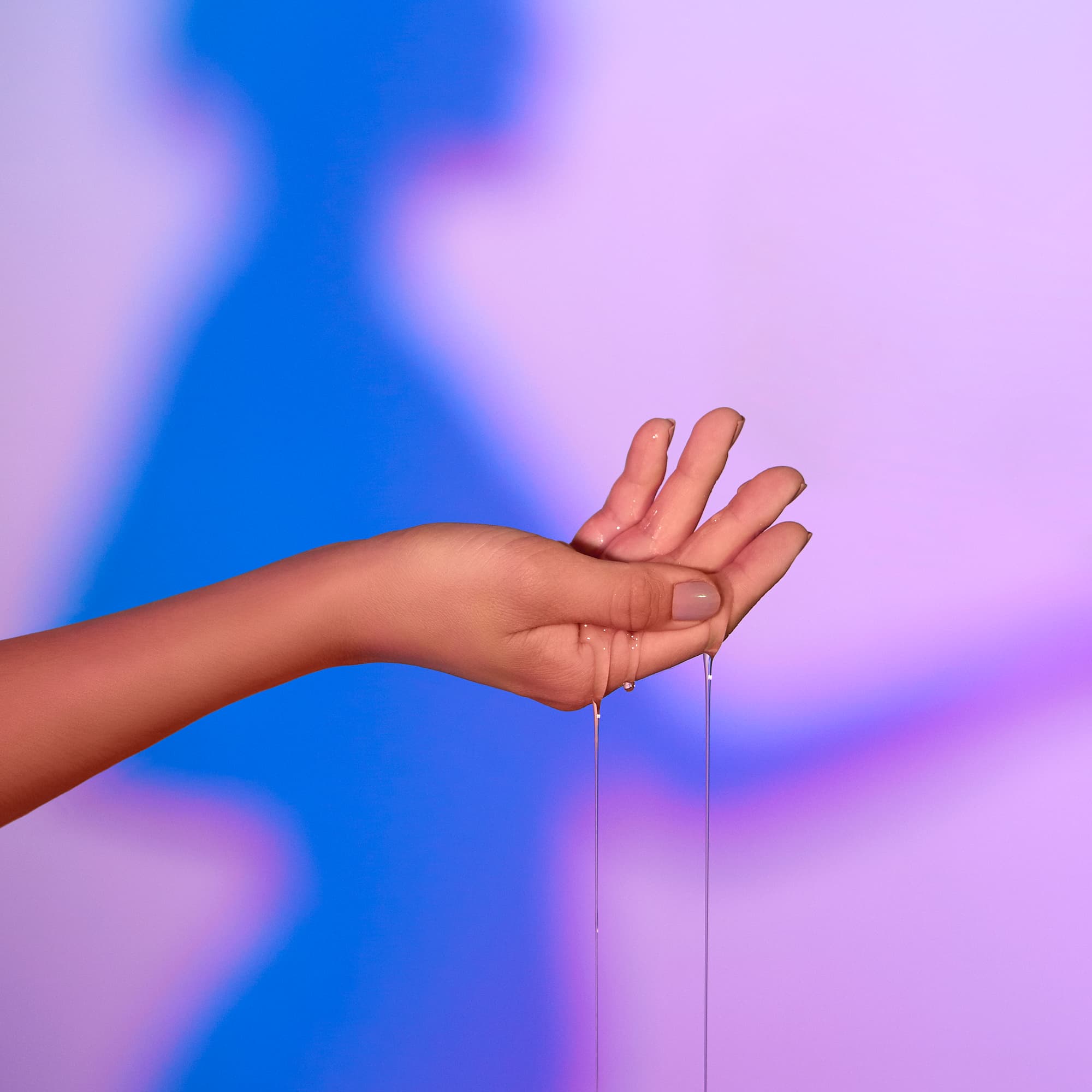A hand holds a bottle of vanilla warming massage oil with liquid dripping from fingers.