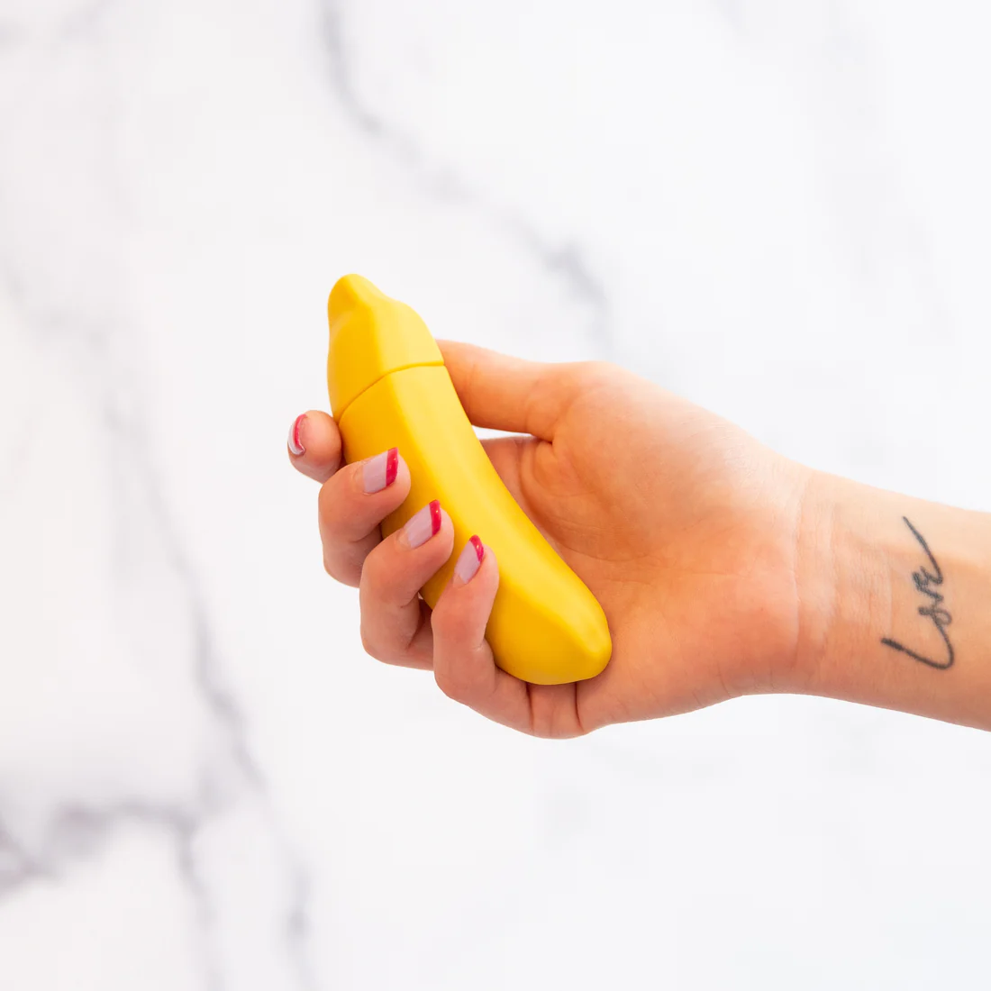 A yellow banana-shaped vibrator held in a hand with a "love" tattoo.