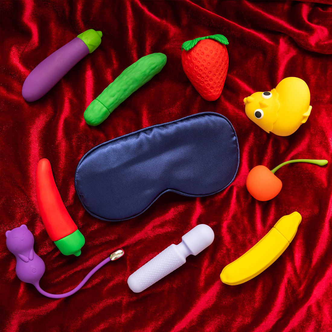 A navy blue satin sleep mask lies on a red velvet surface surrounded by novelty items.