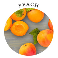 A circular image of several whole and halved peaches with mint leaves on a gray wooden surface.