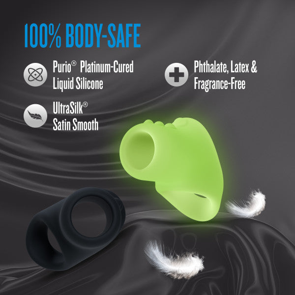 Two silicone cocksling rings, one black and one glowing green, on a dark satin background.