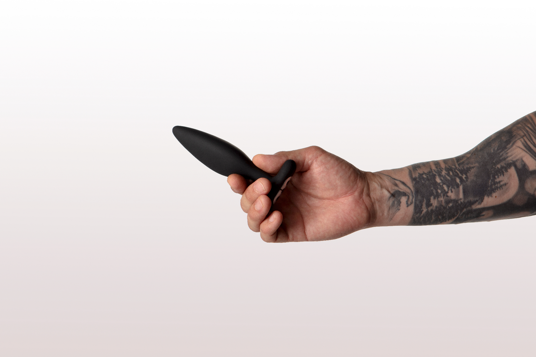 A hand with tattoos holds a black vibrating anal plug.