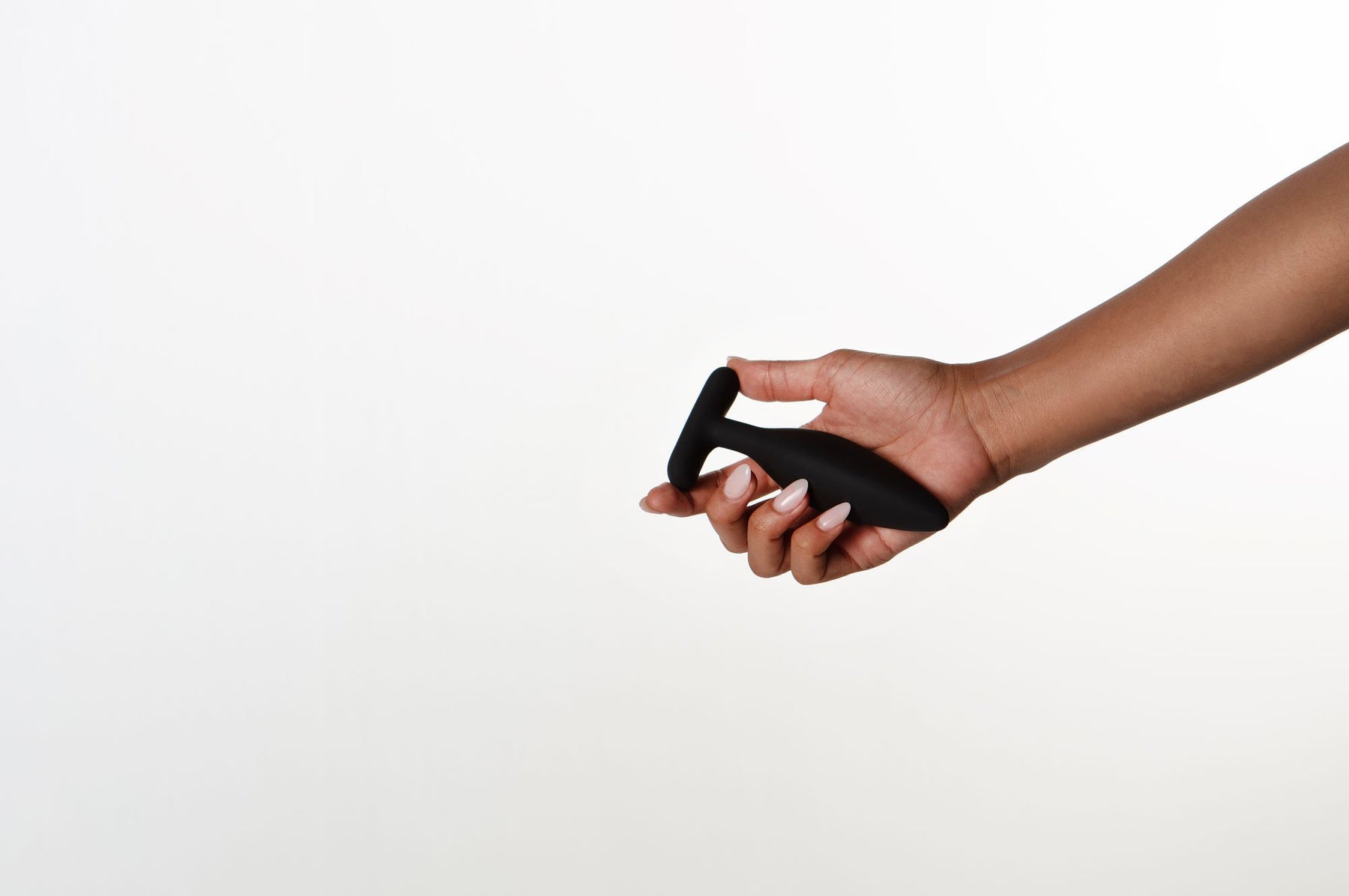 A hand holds a black vibrating anal plug with a T-shaped base.