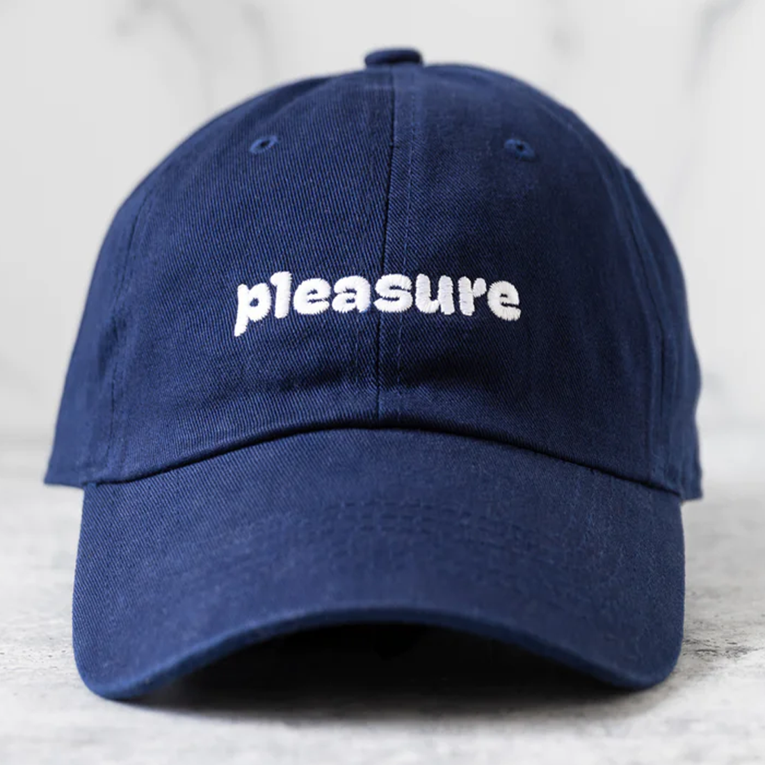 Navy blue cotton dad hat with "pleasure" embroidered in white.