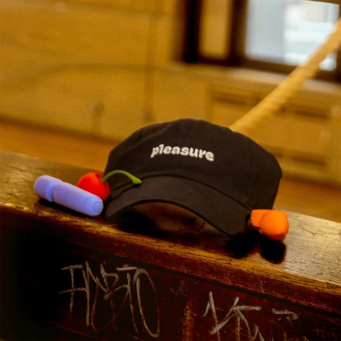 Black dad hat with "pleasure" embroidered in white, a cherry charm, and a purple vibrator.