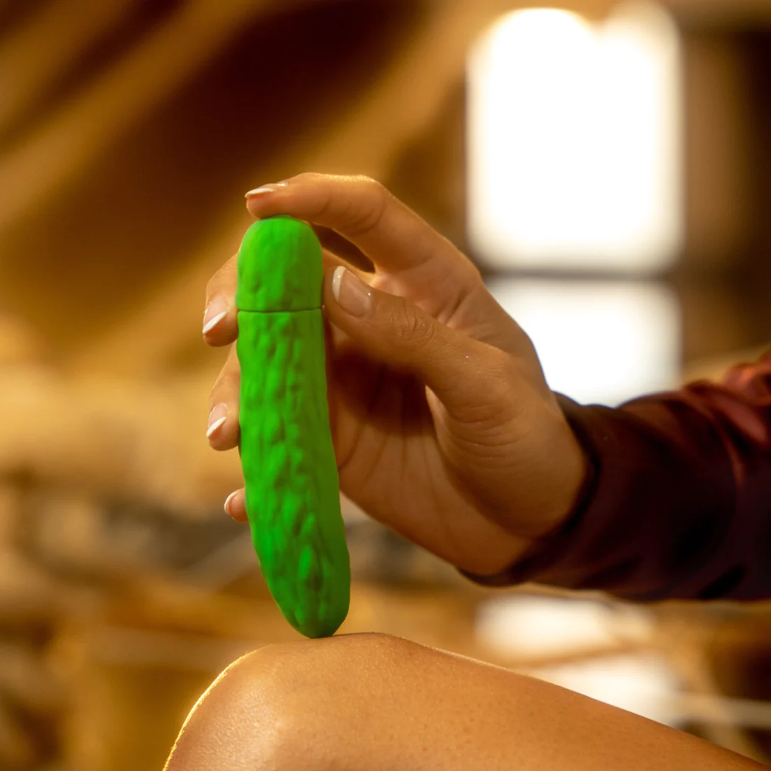 Green pickle-shaped vibrating bullet massager held by a hand.