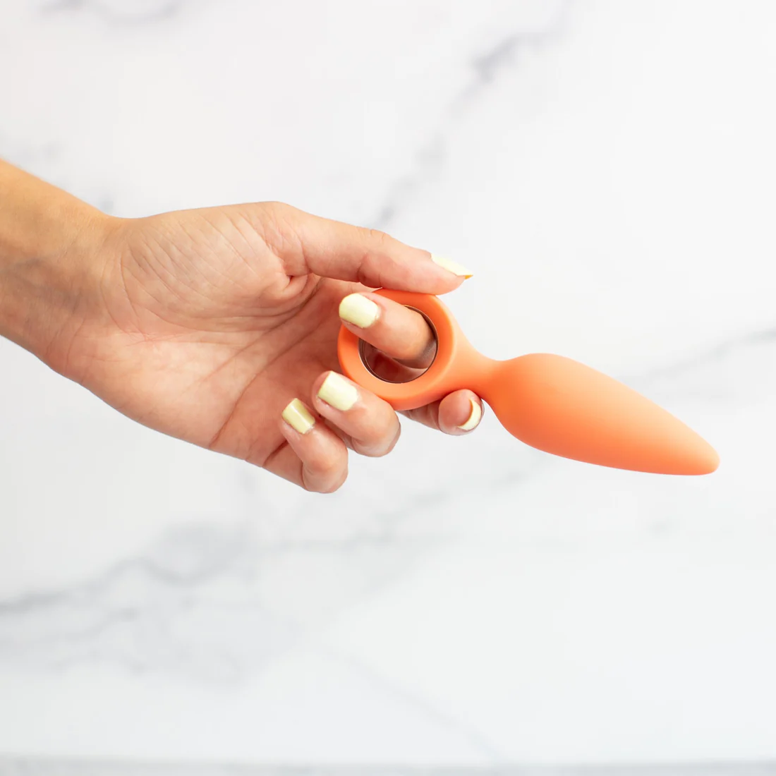 Orange silicone butt plug with a finger loop held by a hand.