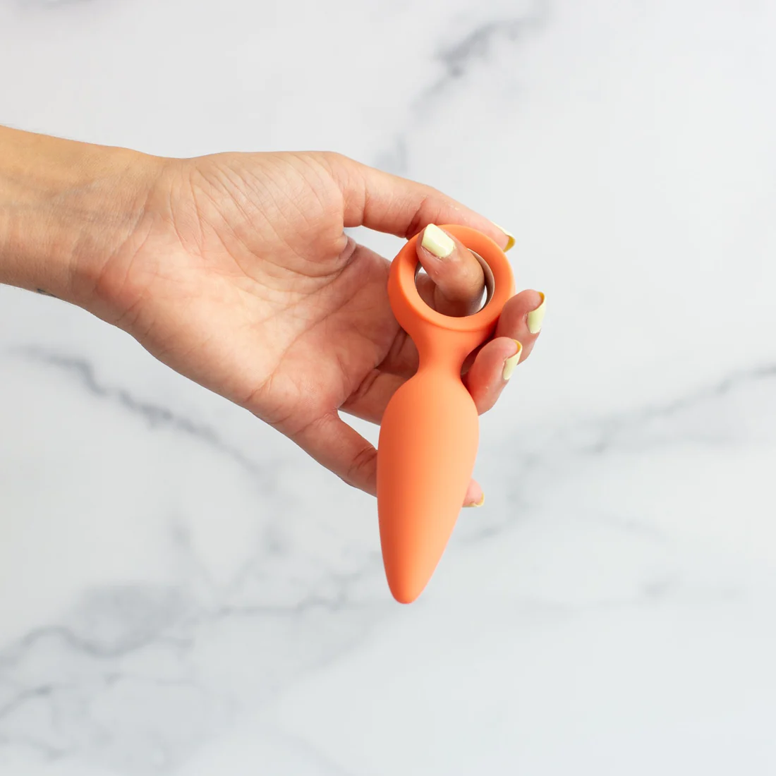 Orange silicone butt plug with a ring handle held by a hand.