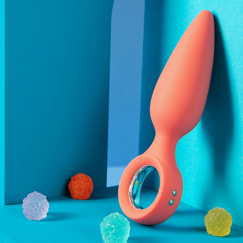 A peach-colored vibrating butt plug with a loop handle and three small silver buttons.