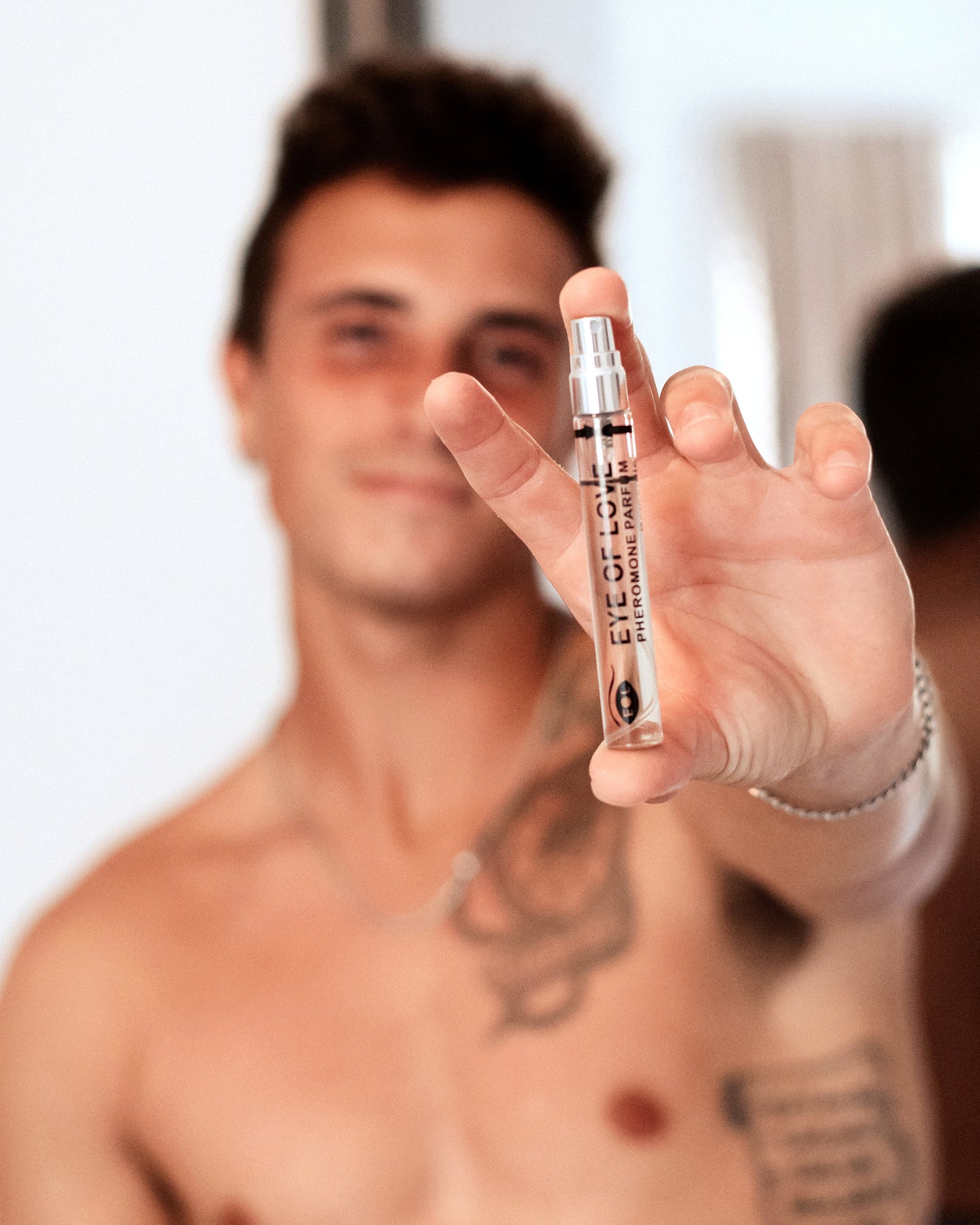 A man holds a small bottle of Eye of Love Confidence Pheromone Cologne.