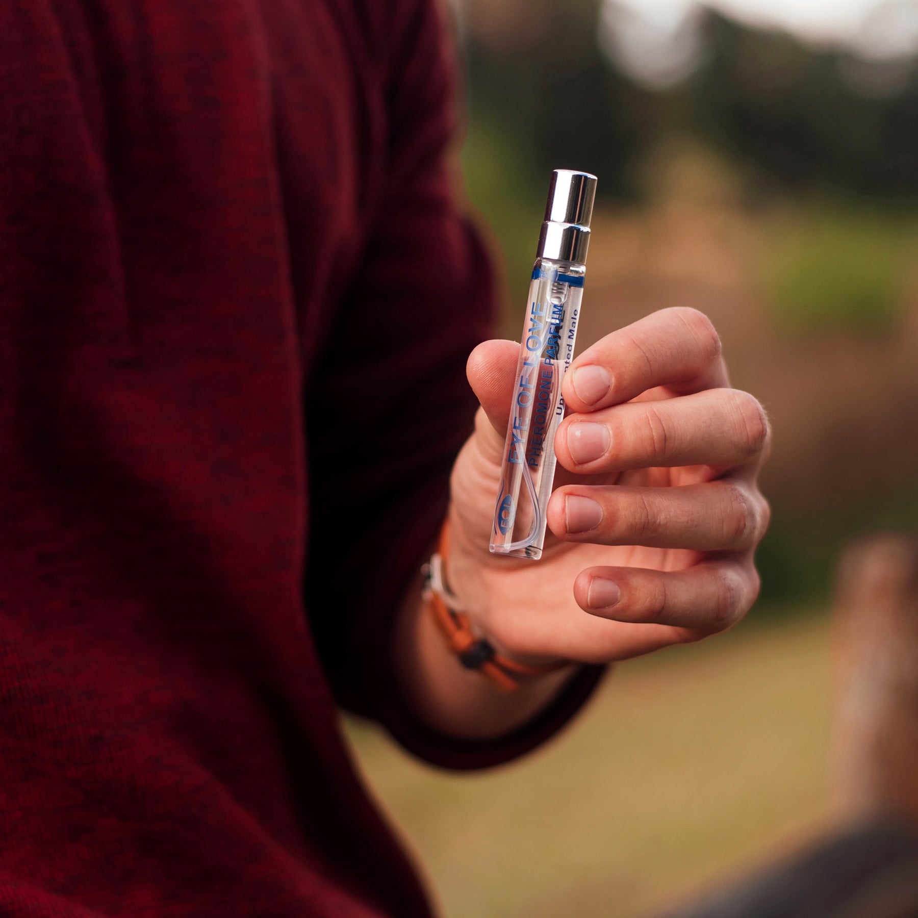A hand holds a small, clear glass vial of unscented pheromone oil for men.