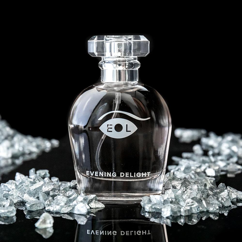 A clear glass perfume bottle with a faceted cap, labeled "Evening Delight" and "EOL".