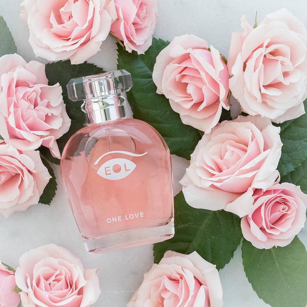 A bottle of One Love perfume surrounded by pink roses.