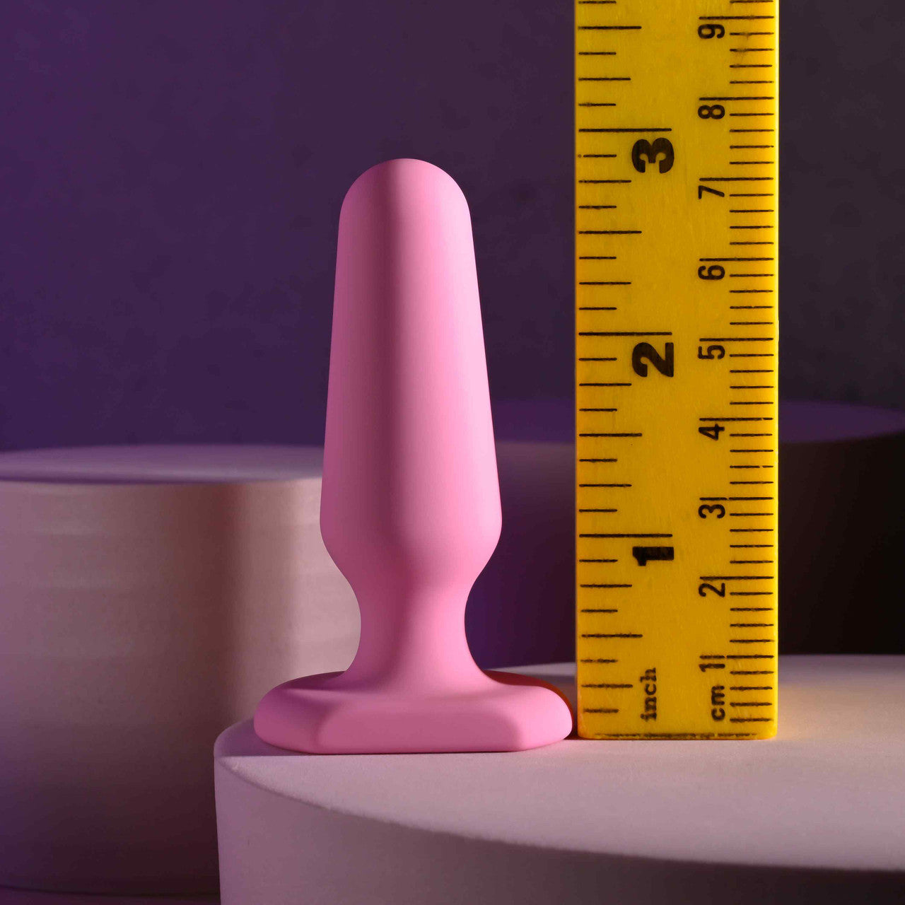 Pink silicone anal plug with a flared base, measured against a ruler.