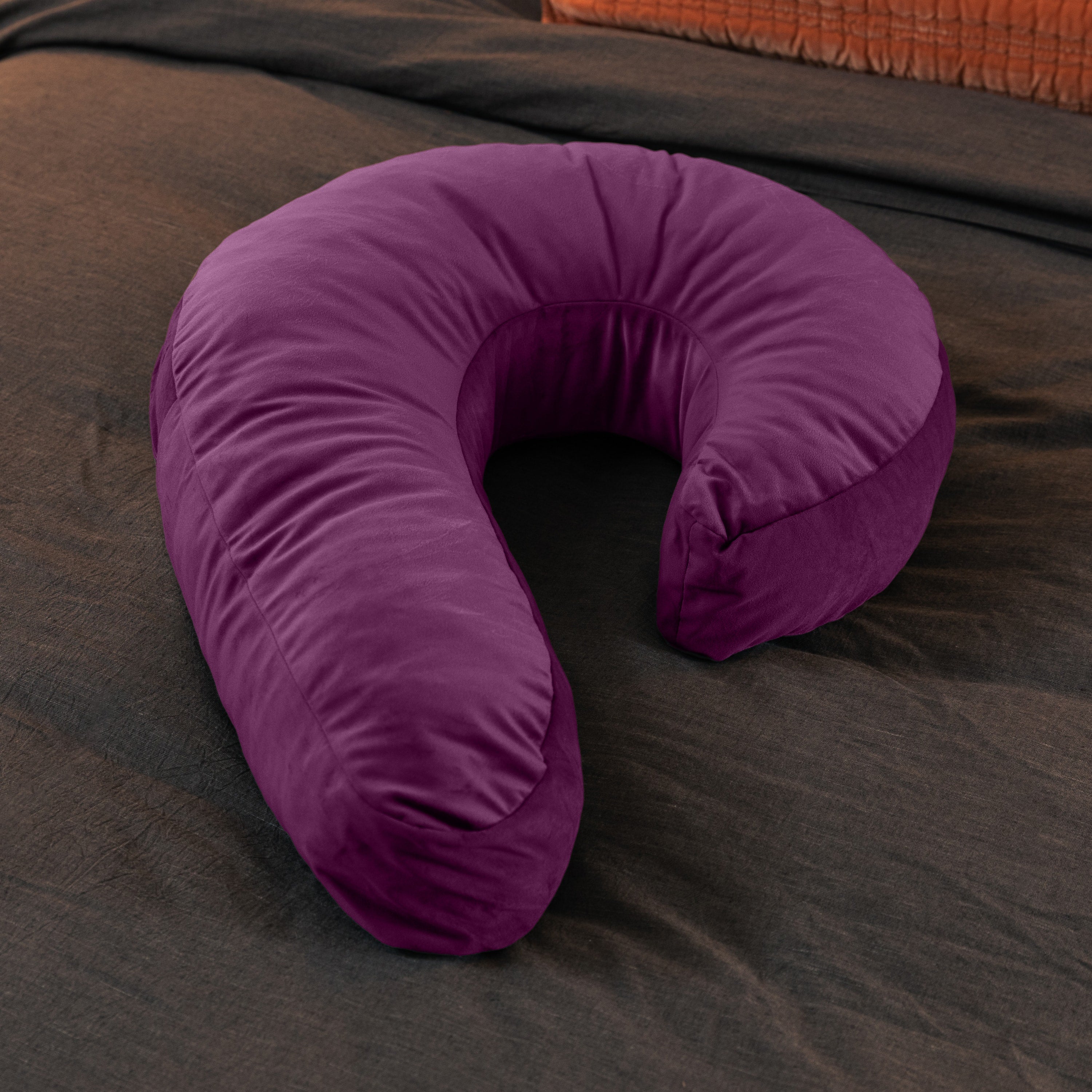 A purple horseshoe-shaped pillow made of memory foam rests on a dark textured surface.