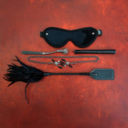 BDSM kit with blindfold, clamps, pinwheel, feather tickler, and paddle.