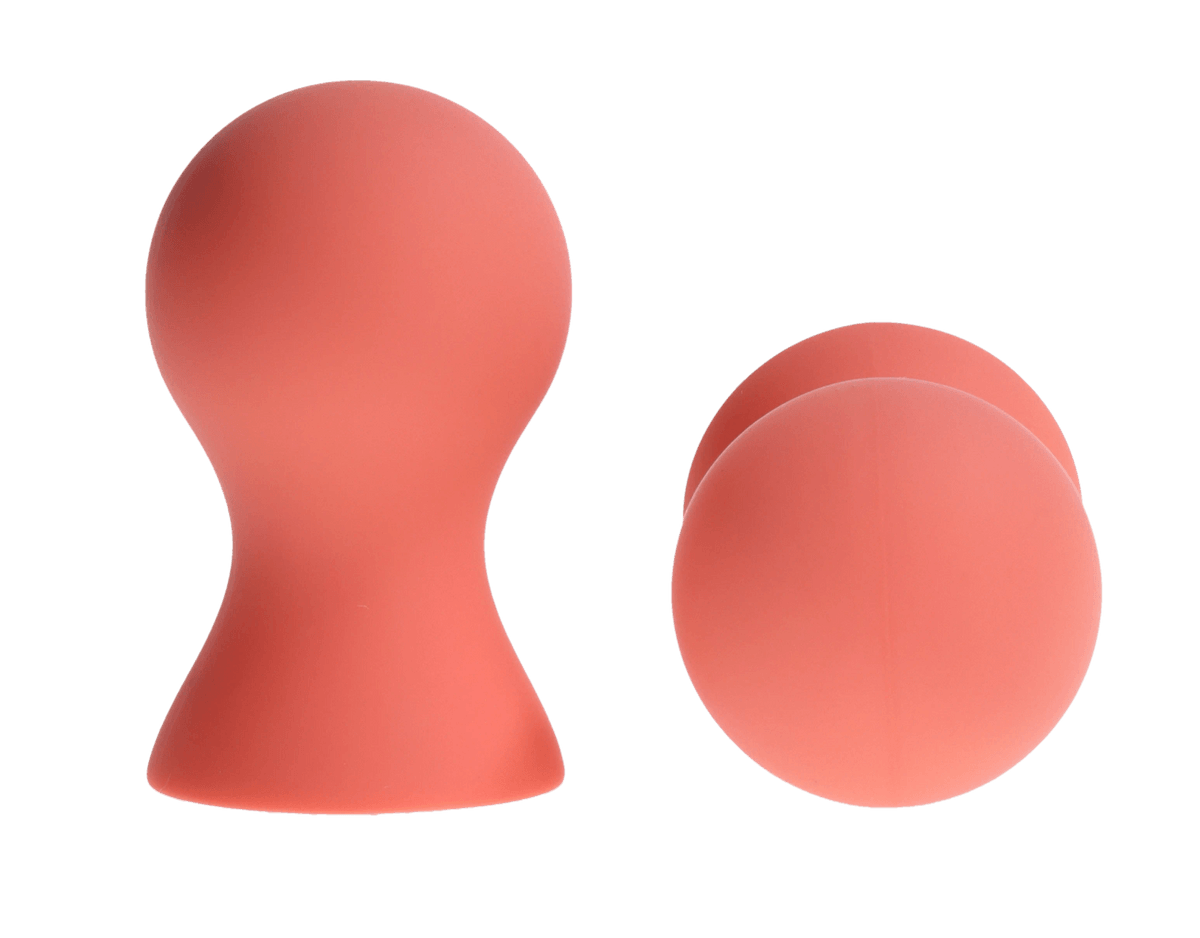 Two coral-colored silicone nipple suckers on a green background.
