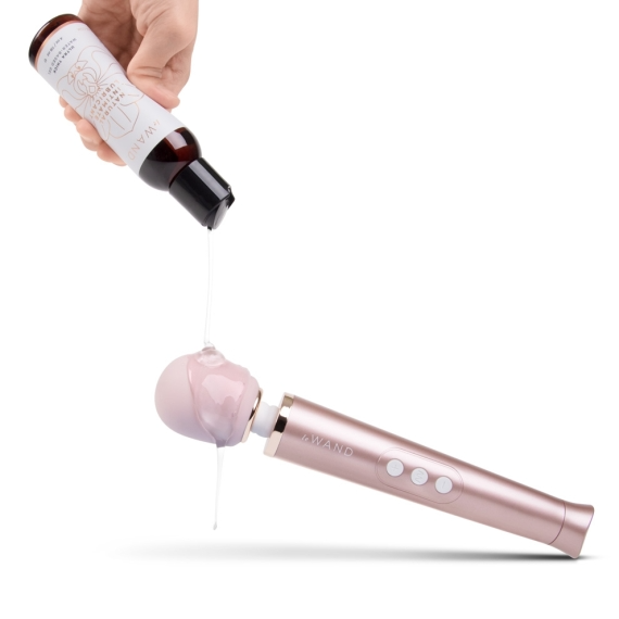 A hand pours natural water-based lubricant onto a rose gold vibrator.