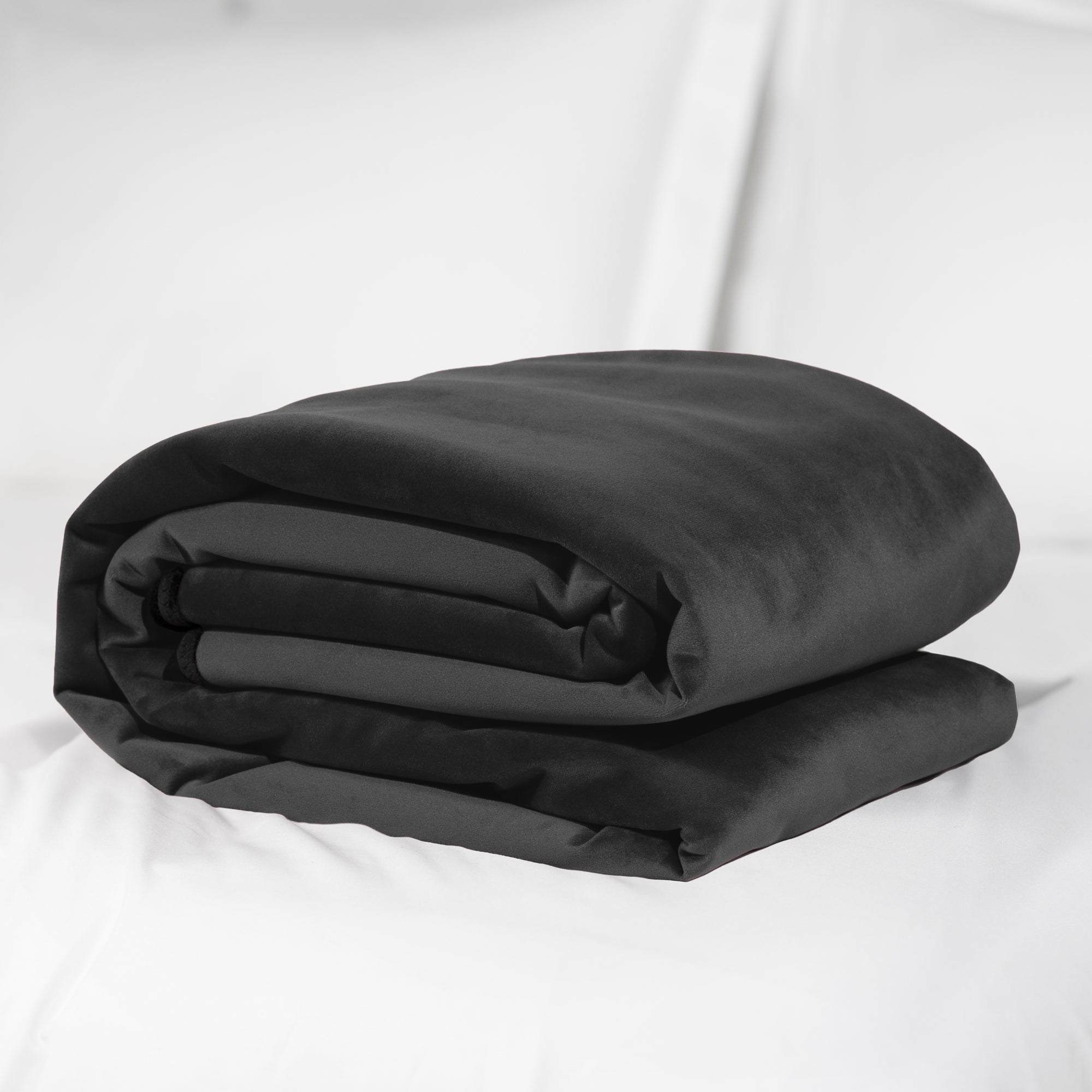A folded black microvelvet blanket lies on a white surface.