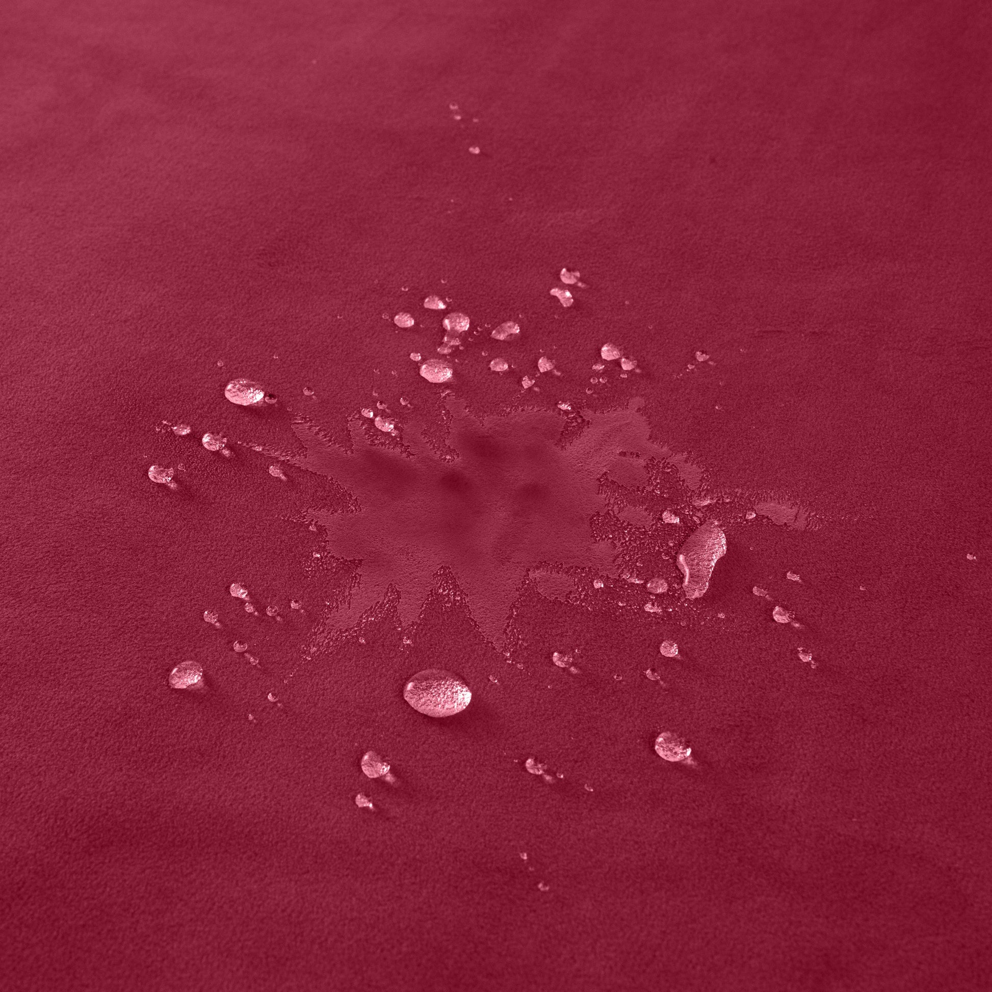 A merlot colored waterproof microvelvet throw with water droplets on its surface.