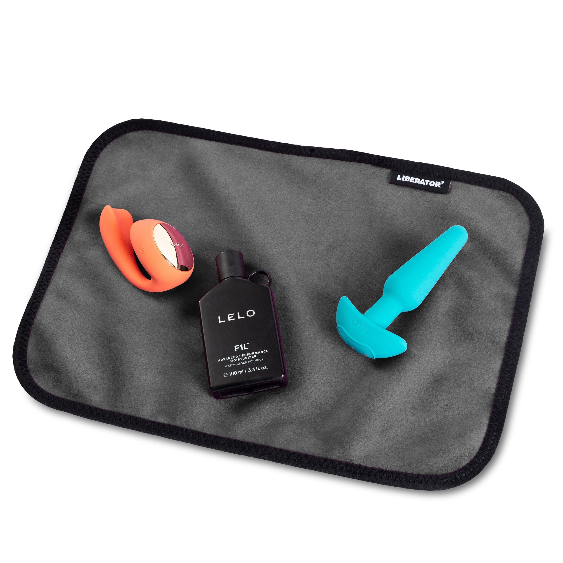 A moisture-proof toy pad with a vibrator, a bottle of LELO F-1L moisturizer, and another toy on a gray mat.