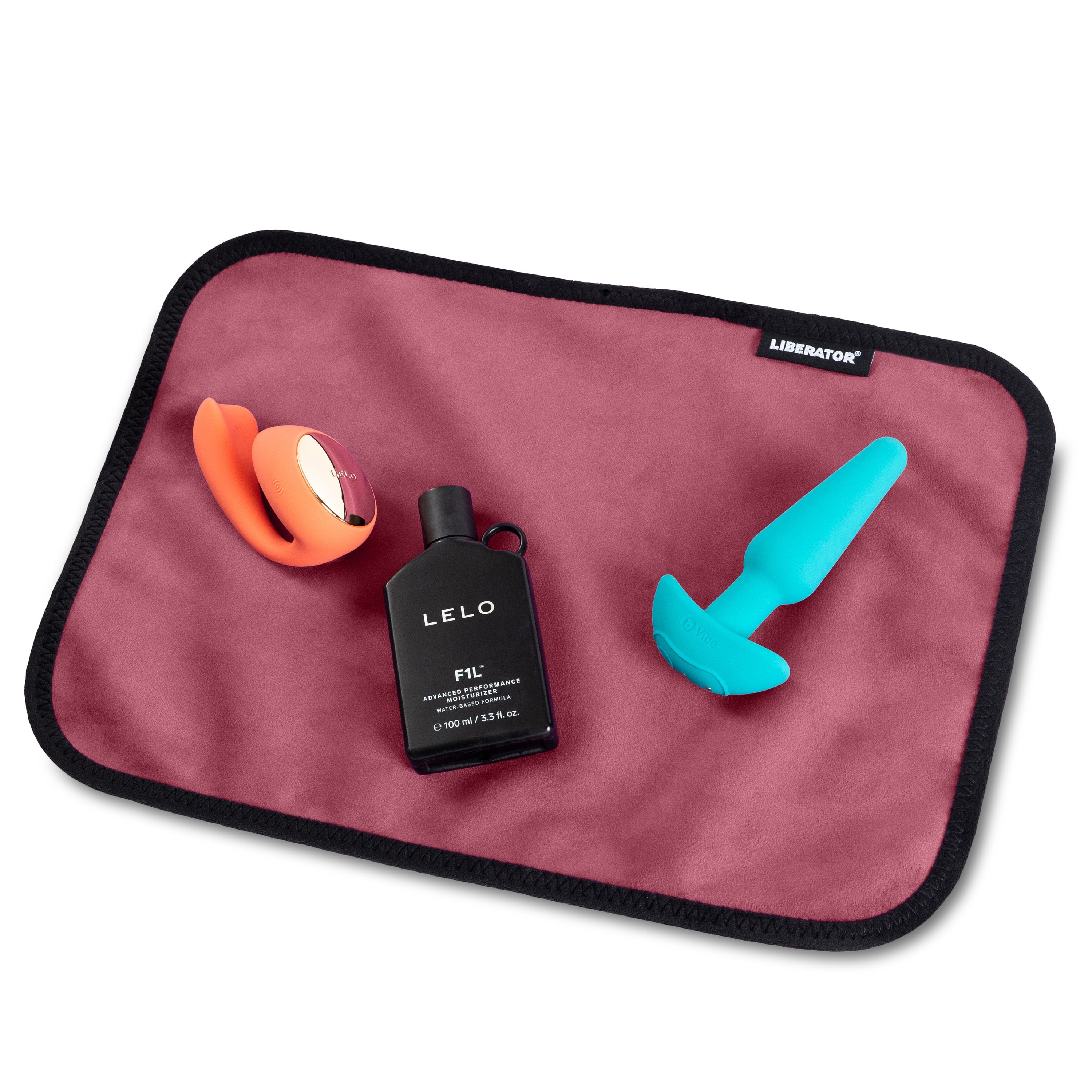 A pink Liberator moisture-proof toy pad with a vibrator, a bottle of LELO F1L moisturizer, and a blue plug.