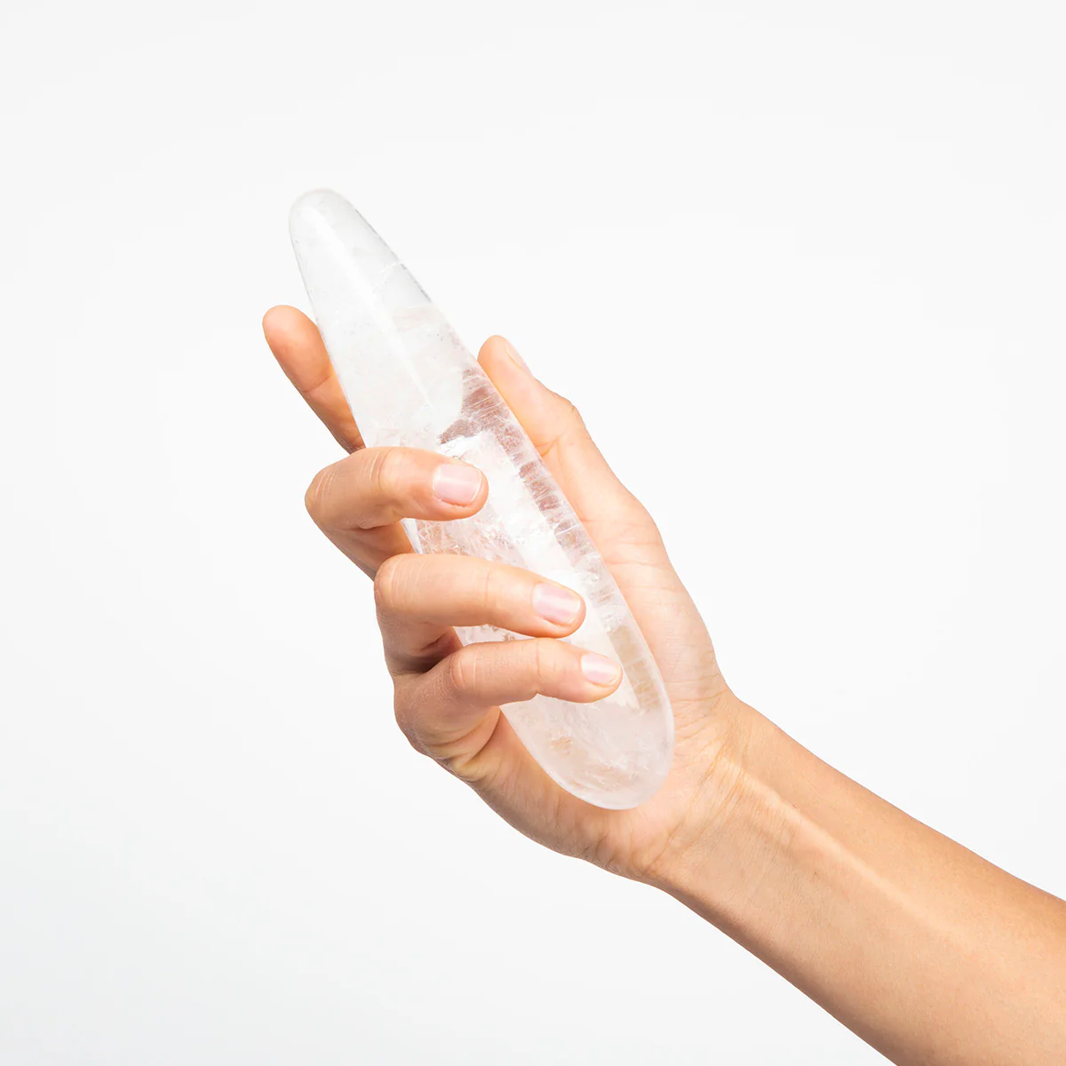 A hand holds a clear quartz crystal wand with a tapered end.