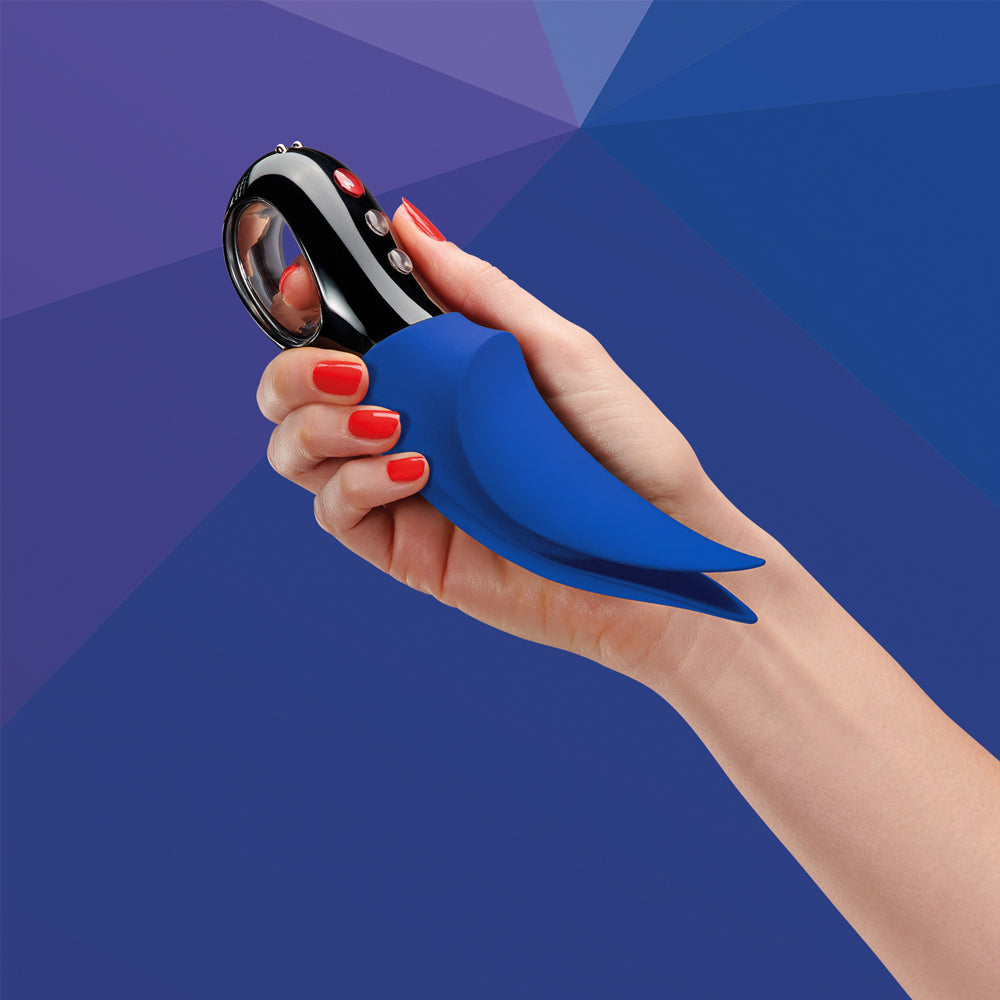 A hand holds a sapphire blue clitoral vibrator with a black loop handle.