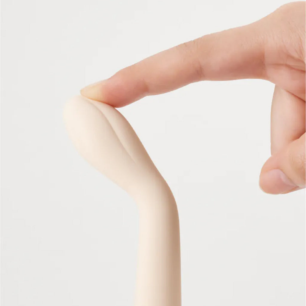 A finger presses on the soft, beige tip of a slim vibrator.