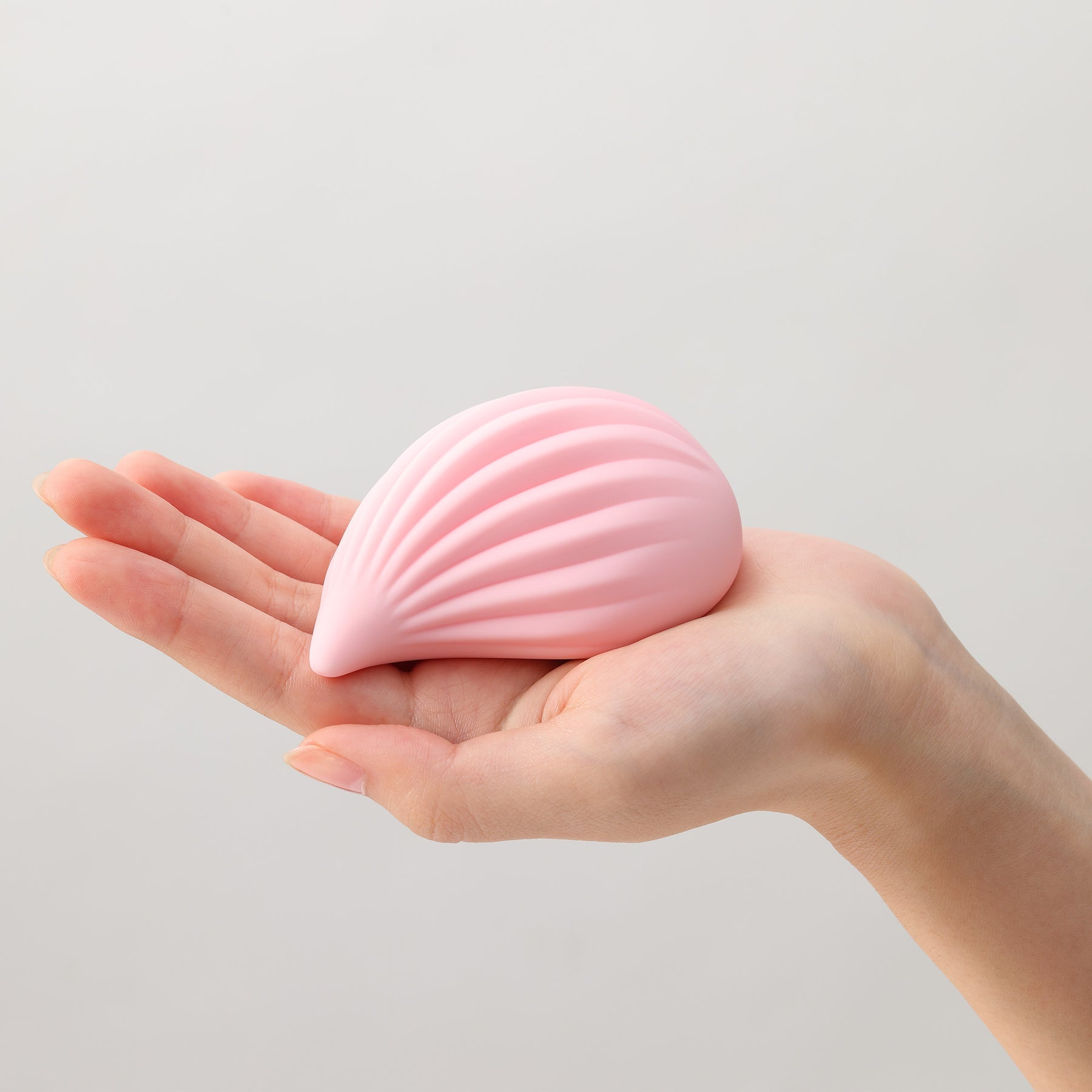 A pink ribbed silicone vibrator rests in a person's palm.