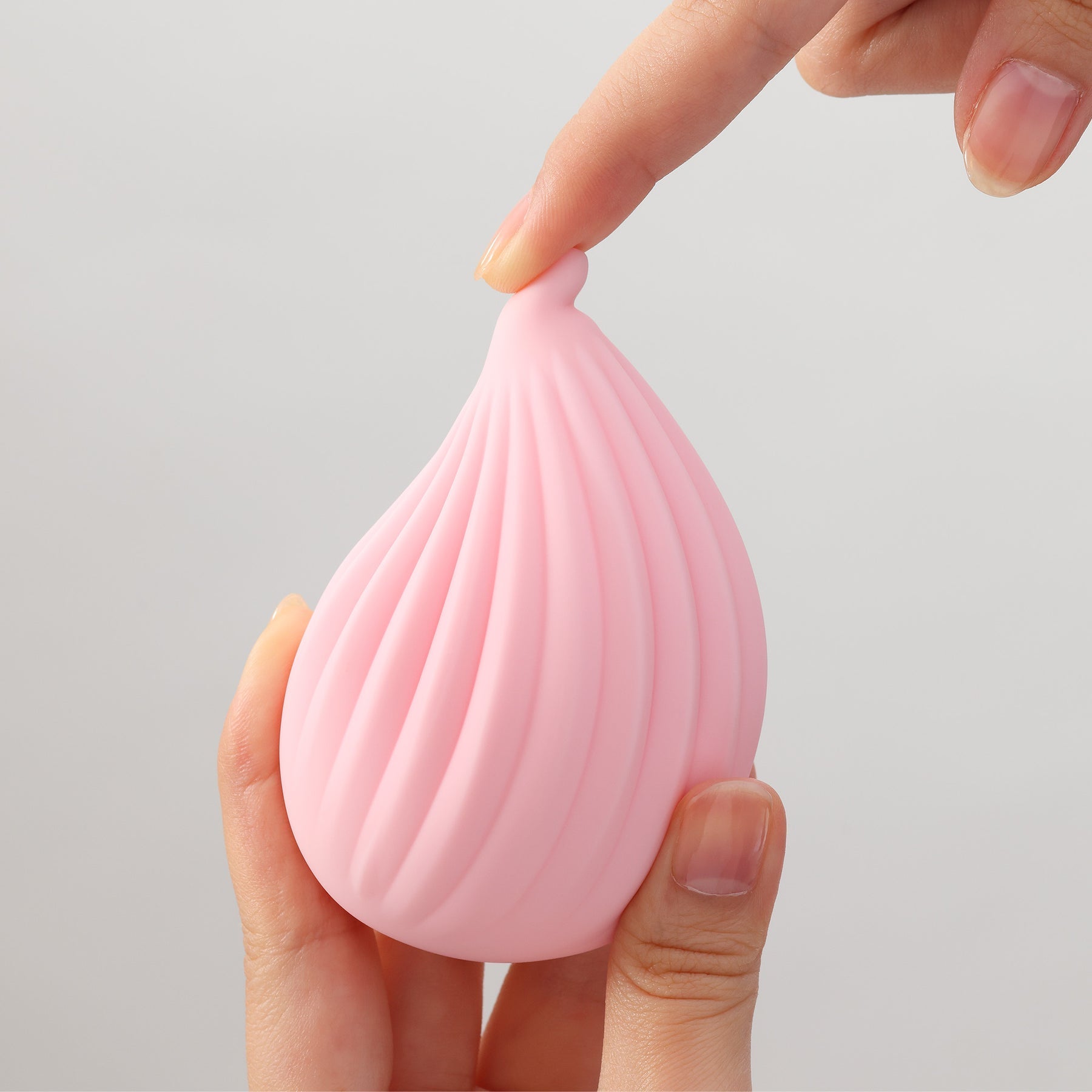 A pink ribbed silicone vibrator held by two hands.