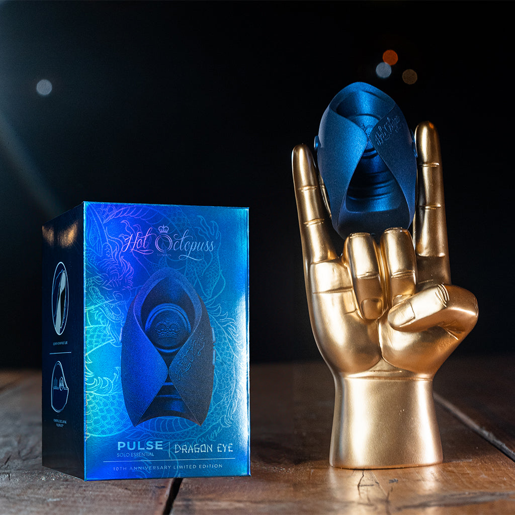A blue vibrator rests in a golden hand next to its matching box.