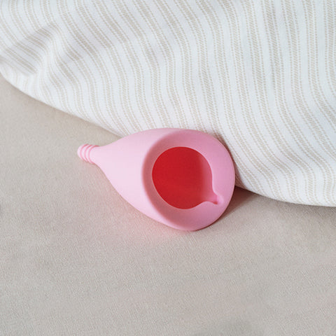 A pink Lily Cup menstrual cup with a ribbed stem rests on a textured surface.
