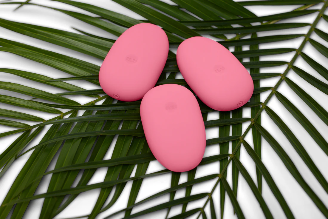 Three pink pebble-shaped vibrators on green palm leaves.